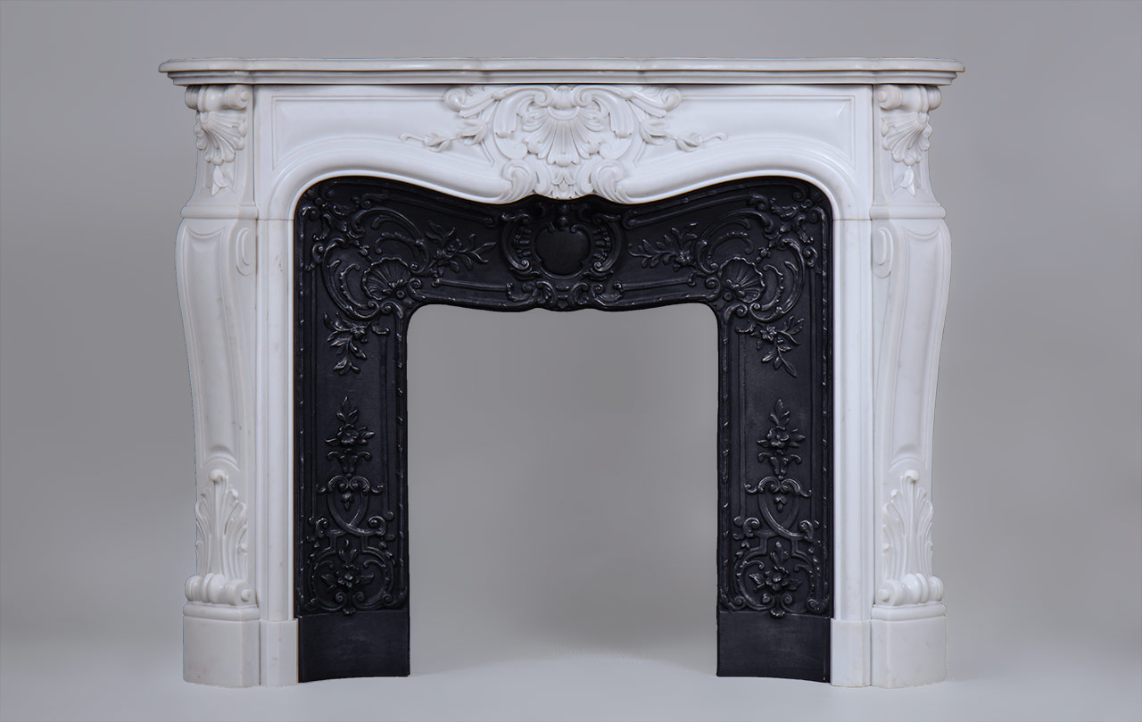 “Madame Du Barry” is a custom-made Louis XV style marble fireplace of a rare opulence.
The generously curved shape is elaborately decorated with finely carved plant motifs. The center of the entablature of this custom fireplace is decorated with a large floral shell, a motif that we find again on the tops of the jambs. The jambs, feature a curved shape, and a rolled up design towards the top.
