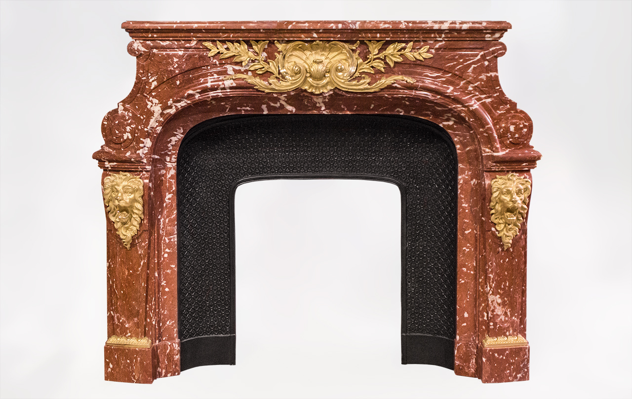 This extraordinary antique fireplace was inspired by the one in the Meeting room of the Fenaille mansion created by Maurice Fenaille in Severac le Chateau, South of France, in 1912.Made out of Red languedoc marble, this fireplace is garnished with sublime gilt bronze ornaments with lions heads and a large foliaged shell.Louis XIV style , this fireplace is inspired from the fireplace which is in the Salon of Hercule in the Versailles Palace.Both sides of this fireplace are ornated with bronze and are paneled.