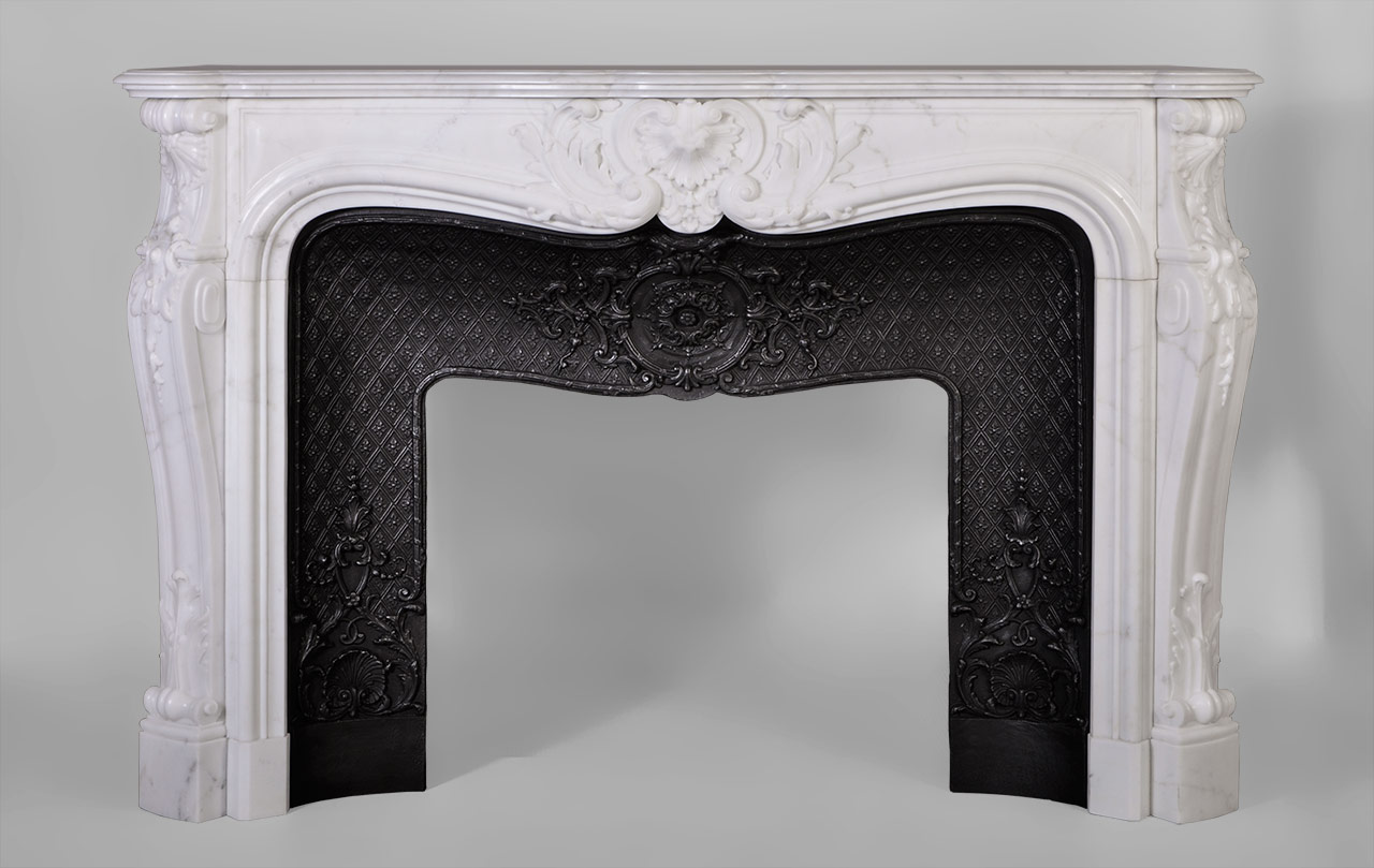 Louis XV style, the carved decoration of this fireplace is extremely elaborate. A large reversed foliaged shell adorns the center of the frieze. Jambs are   curved and have a winding lined with fleshy acanthus leaves in the lower part. The top of the jambs are ornated with carved shells and bells fall.This fireplace is equipped with a beautiful cast iron insert adorned with scrolls, shells and foliage medallions .