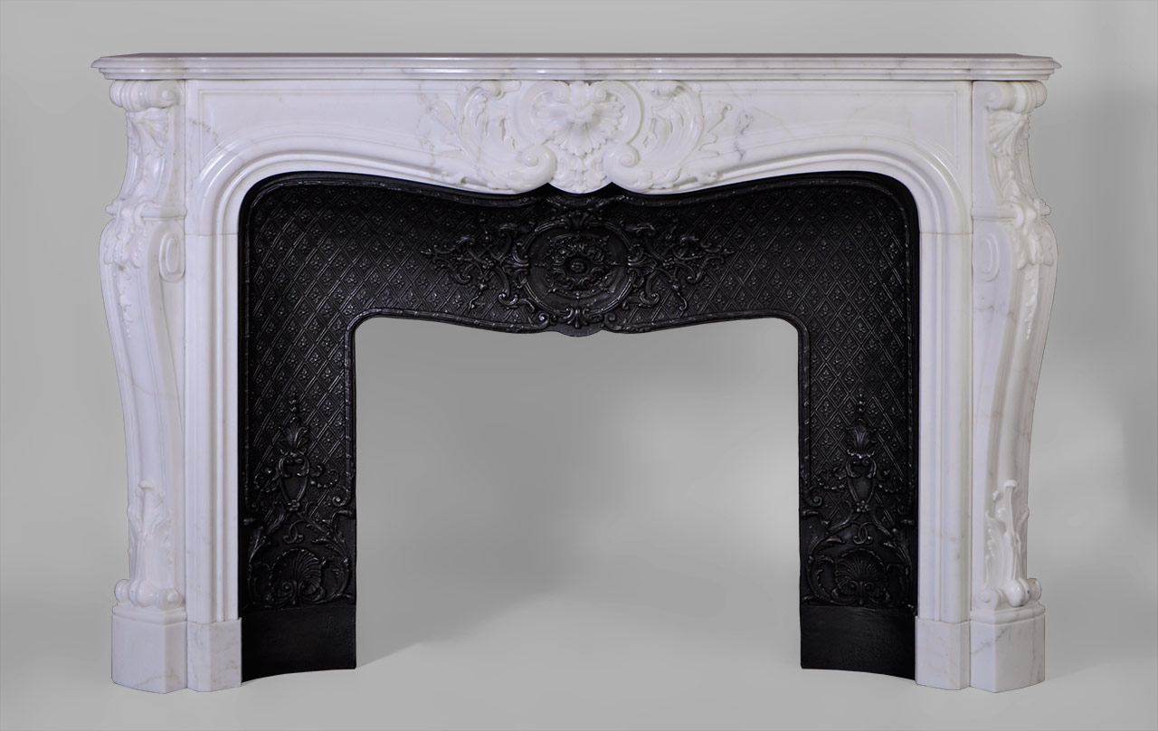 Louis XV style, the carved decoration of this fireplace is extremely elaborate. A large reversed foliaged shell adorns the center of the frieze. Jambs are   curved and have a winding lined with fleshy acanthus leaves in the lower part. The top of the jambs are ornated with carved shells and bells fall.This fireplace is equipped with a beautiful cast iron insert adorned with scrolls, shells and foliage medallions .
